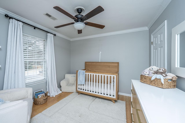 bedroom with hardwood / wood-style flooring, crown molding, a nursery area, and ceiling fan