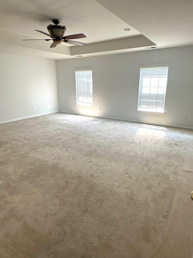empty room with carpet floors, a tray ceiling, ceiling fan, and baseboards