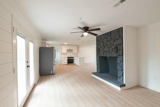 unfurnished living room with a stone fireplace, ceiling fan, and light wood-type flooring