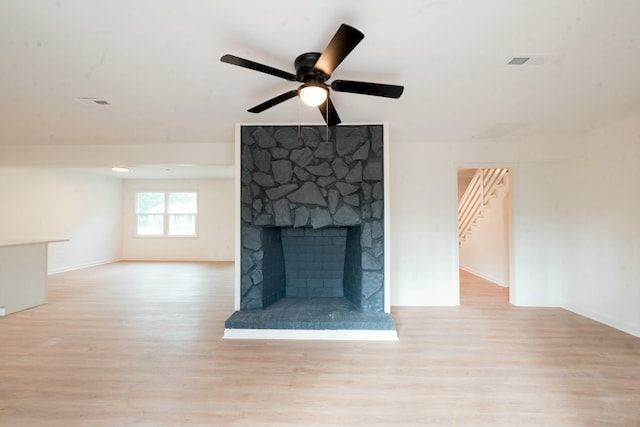 unfurnished living room with light hardwood / wood-style floors, a stone fireplace, and ceiling fan