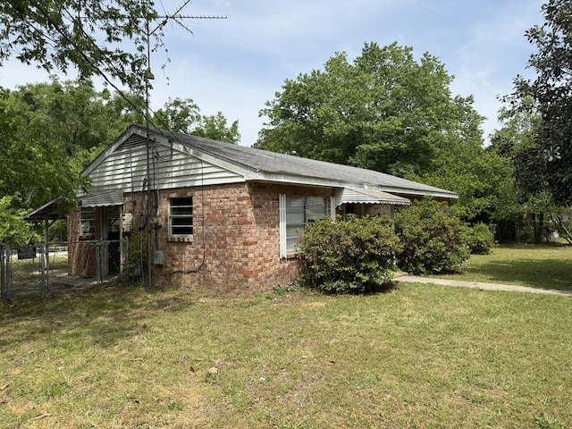 view of side of property with a lawn, fence, and brick siding
