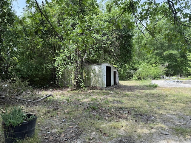 view of yard featuring a forest view, an outdoor structure, and a storage shed