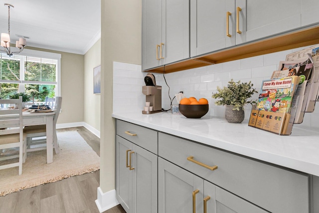 kitchen featuring a notable chandelier, light hardwood / wood-style floors, tasteful backsplash, and gray cabinetry