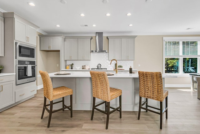 kitchen with appliances with stainless steel finishes, a center island with sink, a kitchen breakfast bar, and wall chimney range hood