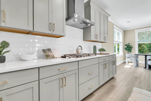 kitchen featuring gray cabinetry, light hardwood / wood-style floors, tasteful backsplash, wall chimney exhaust hood, and stainless steel gas stovetop