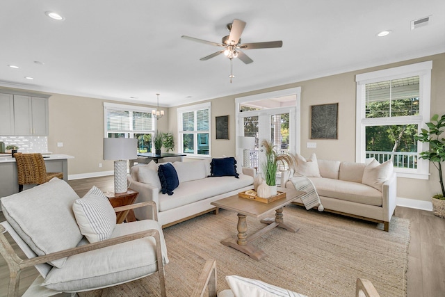 living room with ceiling fan with notable chandelier, light hardwood / wood-style floors, and ornamental molding