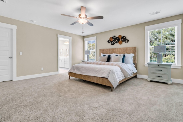 bedroom with ceiling fan, light colored carpet, and connected bathroom