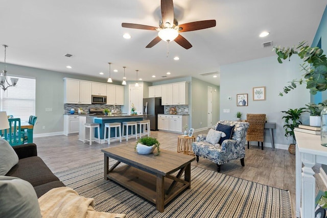 living room with light hardwood / wood-style floors and ceiling fan with notable chandelier