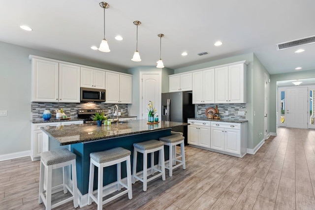 kitchen with white cabinetry, dark stone countertops, decorative backsplash, a kitchen island with sink, and appliances with stainless steel finishes