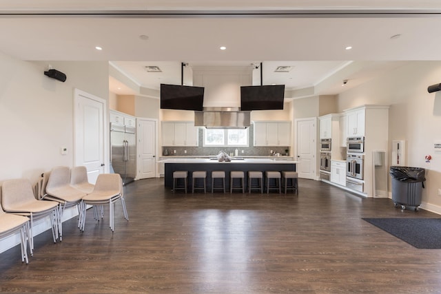 kitchen featuring a center island with sink, stainless steel appliances, a breakfast bar, dark hardwood / wood-style floors, and white cabinetry