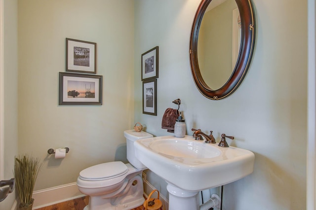 half bath with toilet, baseboards, and wood finished floors