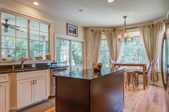 kitchen with stainless steel dishwasher, a sink, dark stone counters, a chandelier, and decorative light fixtures