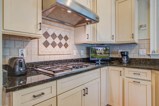 kitchen with exhaust hood, stainless steel gas stovetop, backsplash, and dark stone counters