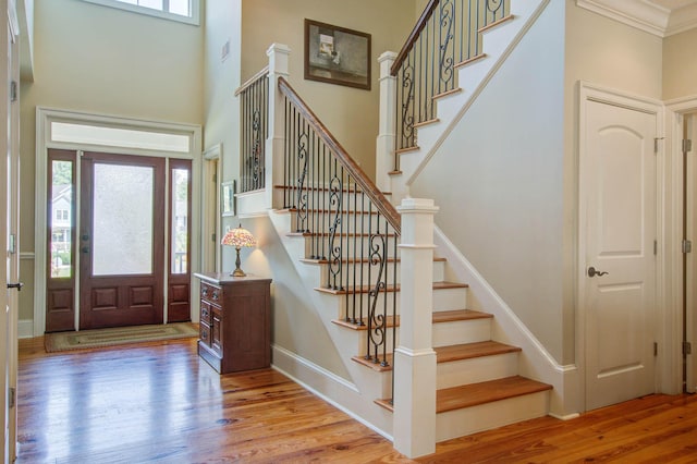entryway with wood finished floors, stairs, a towering ceiling, crown molding, and baseboards
