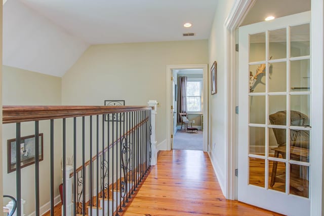 hallway with light wood-style floors, an upstairs landing, vaulted ceiling, baseboards, and recessed lighting