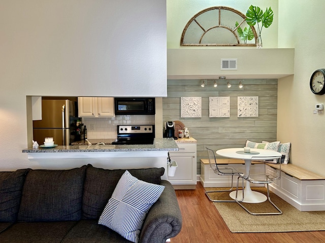 kitchen with wood walls, white cabinetry, backsplash, stainless steel appliances, and light wood-type flooring