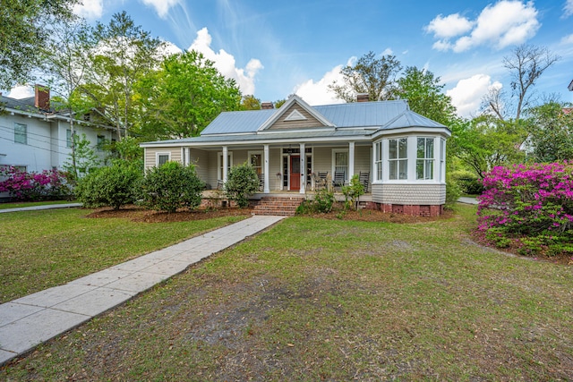 view of front facade with covered porch, a chimney, a front yard, and metal roof