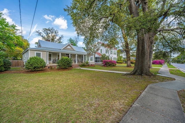 view of front of home featuring metal roof, fence, a chimney, a front lawn, and a porch