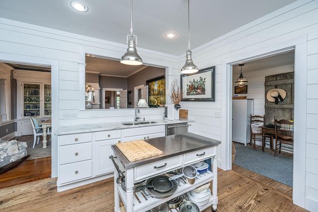 kitchen featuring white cabinetry, light countertops, hanging light fixtures, a sink, and wood finished floors