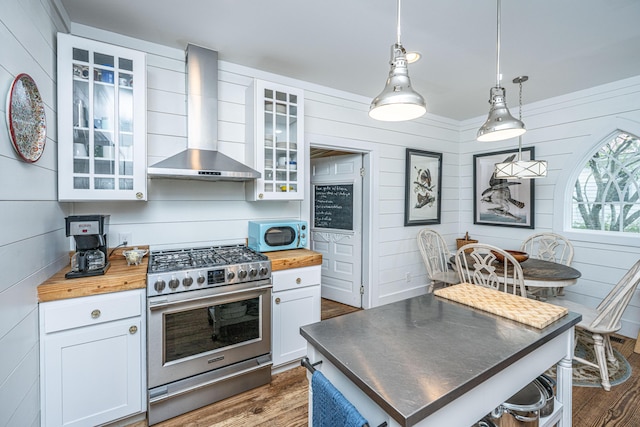 kitchen featuring wood counters, stainless steel range with gas cooktop, white cabinetry, and wall chimney exhaust hood