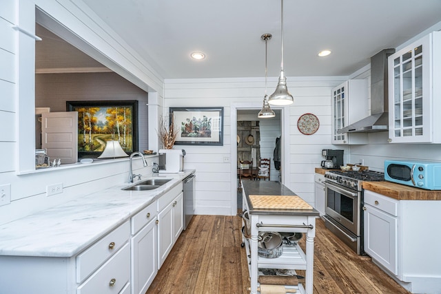 kitchen featuring wall chimney range hood, a sink, stainless steel appliances, and glass insert cabinets