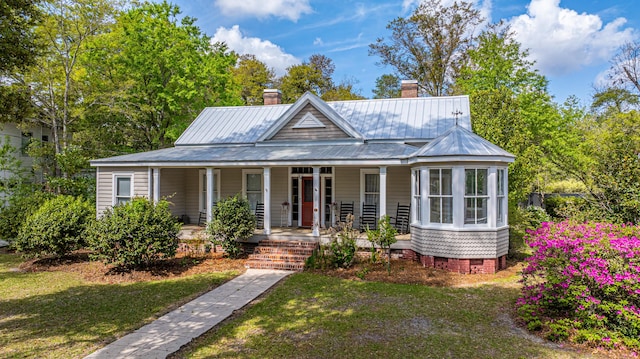 view of front facade featuring a front yard, a chimney, metal roof, crawl space, and a porch