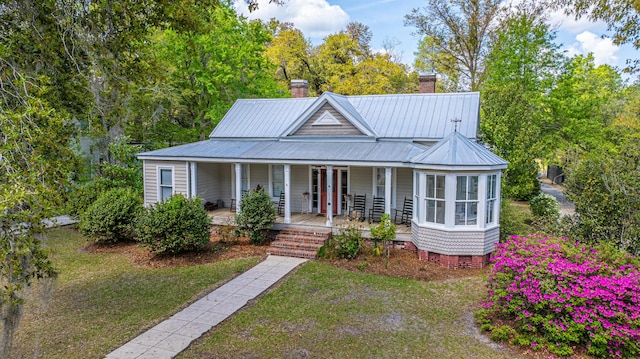 view of front of home with metal roof, a chimney, crawl space, a front yard, and covered porch