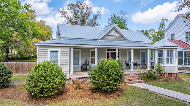 view of front of home featuring metal roof, covered porch, fence, and a chimney
