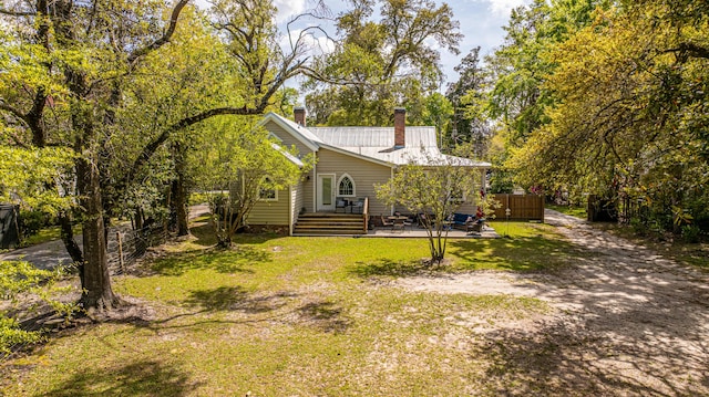 exterior space featuring metal roof, fence, a patio, a chimney, and a lawn
