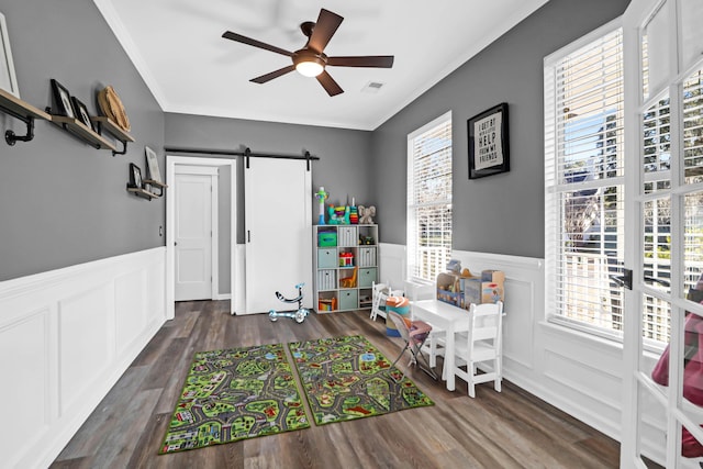 playroom with crown molding, ceiling fan, a barn door, and dark hardwood / wood-style floors