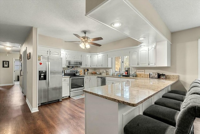 kitchen with dark wood-type flooring, stainless steel appliances, a textured ceiling, white cabinets, and kitchen peninsula