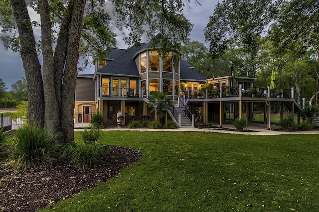 rear view of property featuring a wooden deck, a sunroom, and a lawn