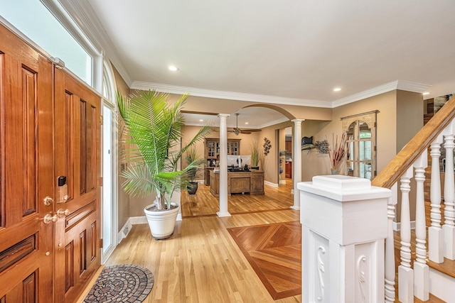 foyer entrance with crown molding, decorative columns, and light wood-type flooring