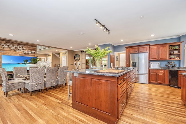 kitchen with appliances with stainless steel finishes, a breakfast bar area, ornamental molding, a kitchen island with sink, and light wood-type flooring