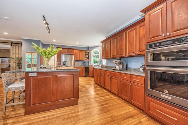 kitchen featuring a breakfast bar area, a center island with sink, light wood-type flooring, appliances with stainless steel finishes, and a barn door