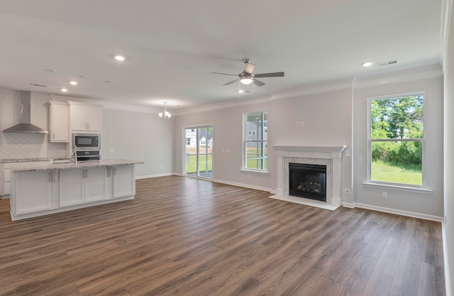 unfurnished living room with ceiling fan with notable chandelier, ornamental molding, a fireplace, and dark wood-type flooring