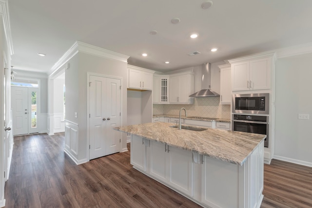 kitchen with white cabinetry, an island with sink, wall chimney exhaust hood, stainless steel appliances, and sink