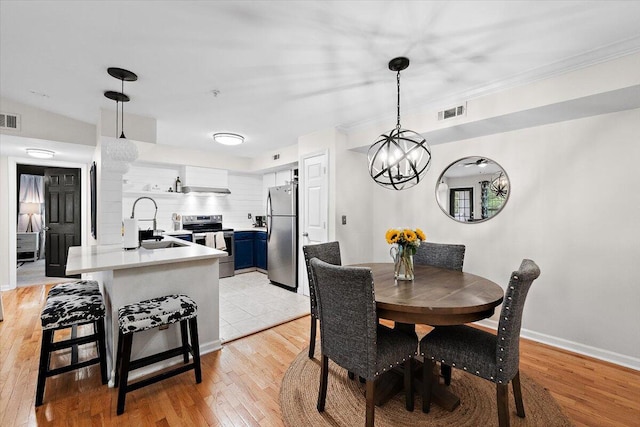 dining area featuring sink, light hardwood / wood-style flooring, a notable chandelier, and vaulted ceiling