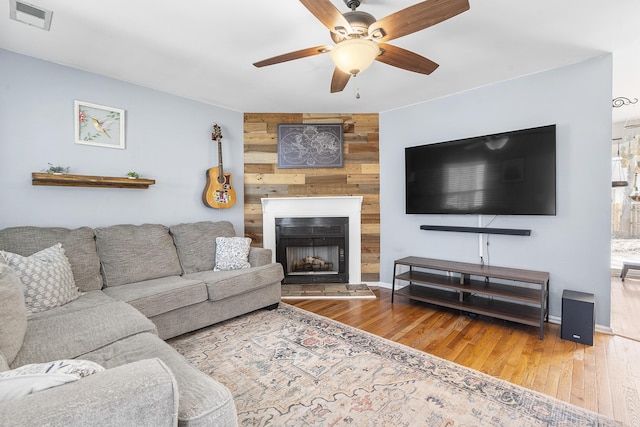 living room featuring a large fireplace, wooden walls, visible vents, a ceiling fan, and hardwood / wood-style flooring