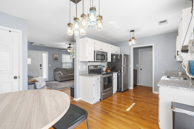 kitchen with stainless steel appliances, visible vents, white cabinetry, a sink, and light wood-type flooring