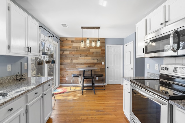 kitchen with appliances with stainless steel finishes, white cabinets, light wood-style floors, and wooden walls