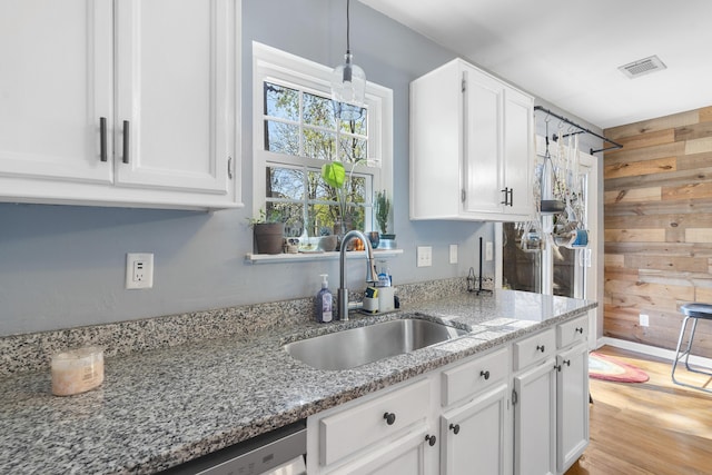 kitchen featuring white cabinetry, wooden walls, visible vents, and a sink