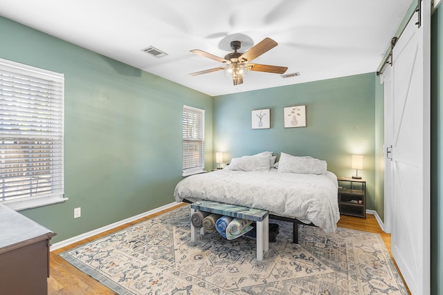 bedroom with visible vents, light wood-style flooring, baseboards, and a barn door