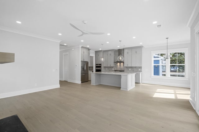 kitchen with open floor plan, wall chimney exhaust hood, appliances with stainless steel finishes, and decorative backsplash