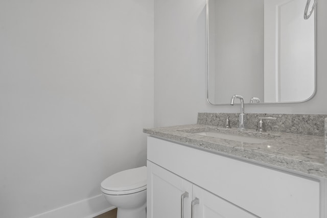 half bathroom with baseboards, vanity, and toilet