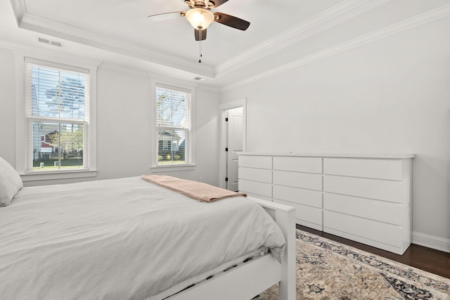 bedroom with a tray ceiling, crown molding, ceiling fan, and dark wood-type flooring