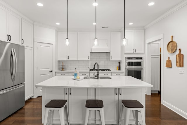 kitchen with appliances with stainless steel finishes, dark hardwood / wood-style flooring, a center island with sink, and hanging light fixtures