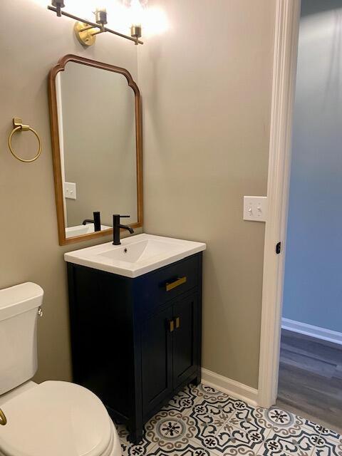 half bathroom featuring tile patterned flooring, toilet, vanity, and baseboards