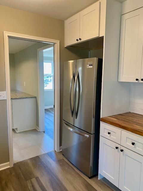 kitchen with light wood finished floors, wooden counters, decorative backsplash, freestanding refrigerator, and white cabinets