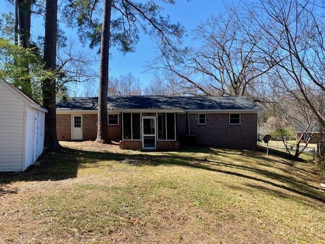 back of property with brick siding, a yard, and a sunroom